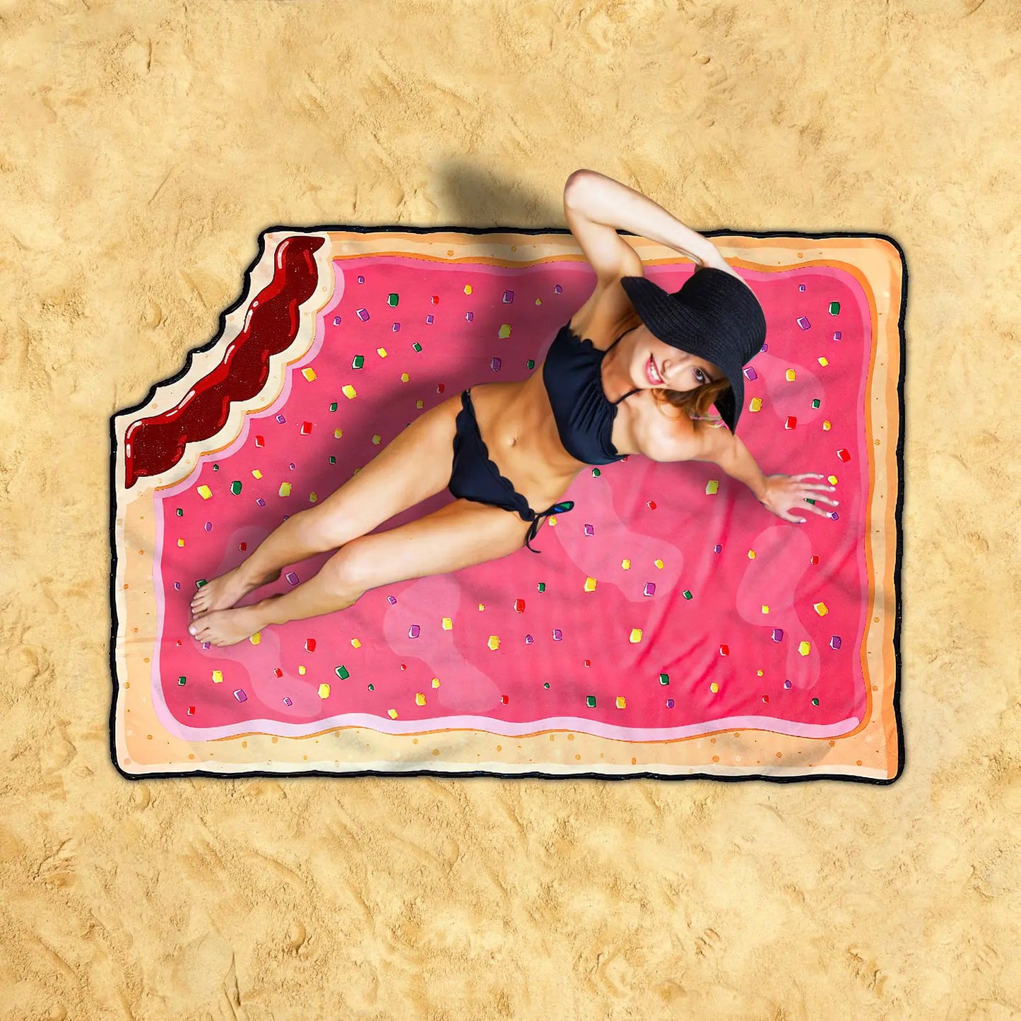 Person lying on a pink inflatable raft shaped like a filled biscuit with sprinkles on a sandy background