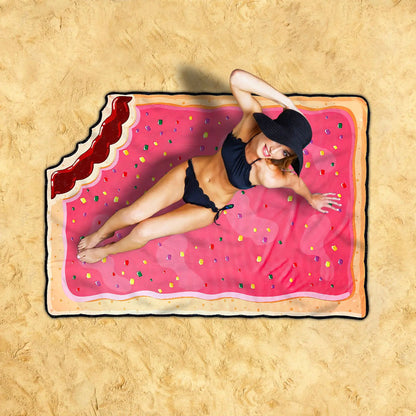 Person lying on a pink inflatable raft shaped like a filled biscuit with sprinkles on a sandy background