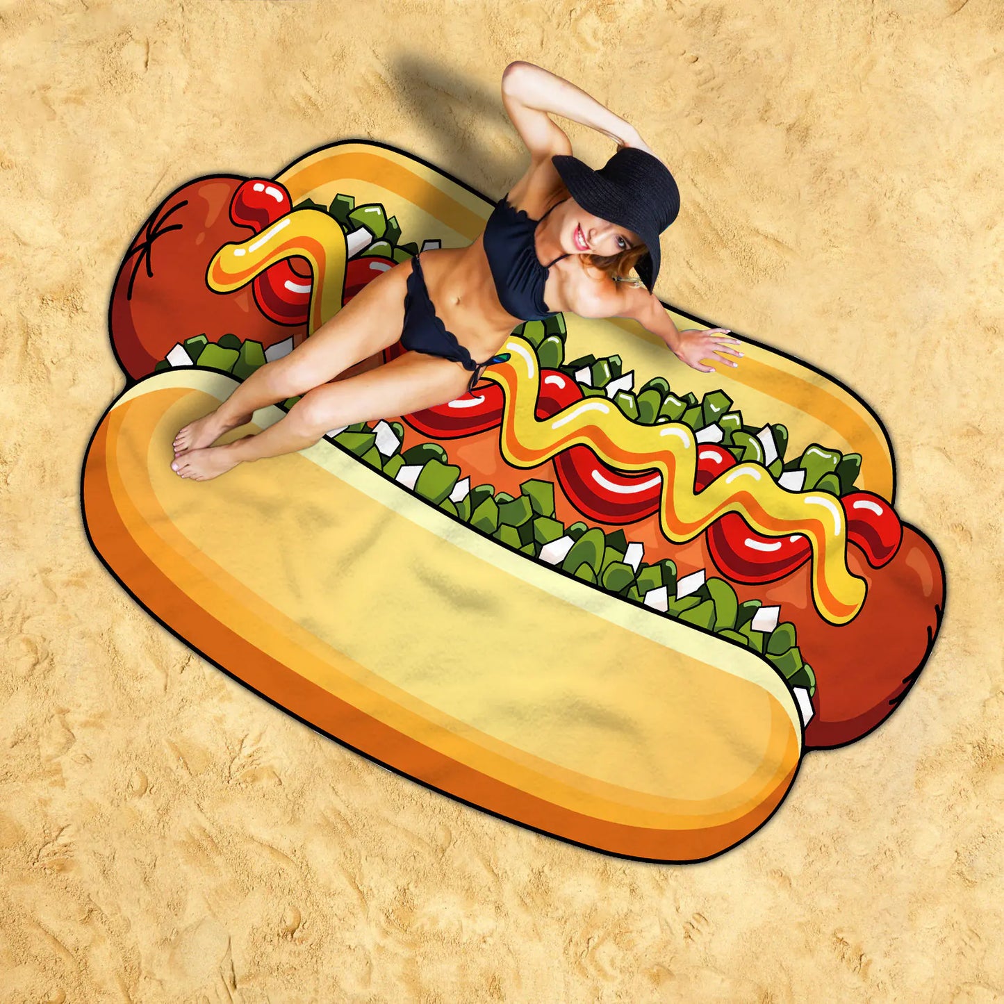 Person lying on a hot dog-shaped beach mat with toppings on a sandy background